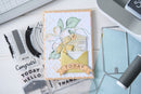 Handmade card with floral design and text on a crafting table with tools.