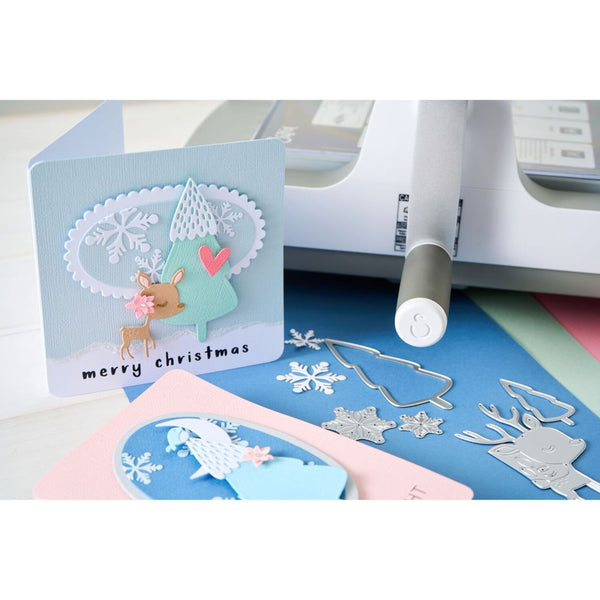 Handmade Christmas card with reindeer design, paper cutter, and craft materials on a white background