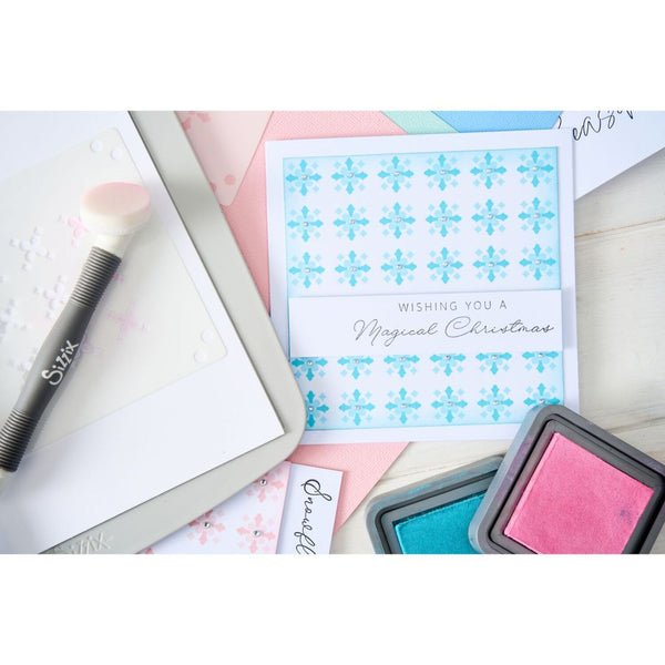 Card with blue snowflakes and text, surrounded by ink pads and a brush on a white background