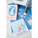 Card with reindeer design and 'merry christmas' text, surrounded by crafting tools on a blue surface.