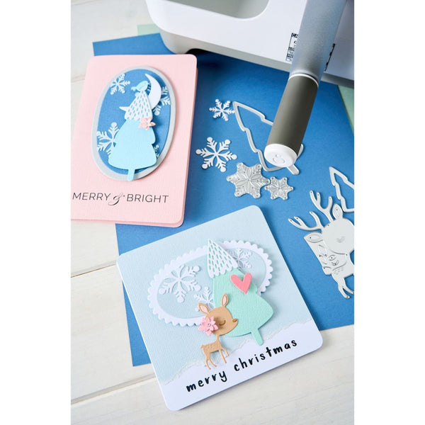 Card with reindeer design and 'merry christmas' text, surrounded by crafting tools on a blue surface.