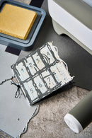 Small metal stamp with numbers on a black mat next to a printer and ink pad.