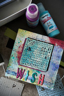 Colorful art project with 'Wish' text and paint bottles on a textured surface