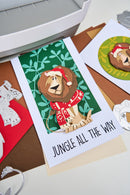Card with a lion wearing a Santa hat and text 'Jungle All The Way' on a table with other cards.