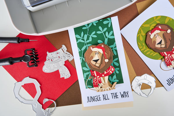 Card with lion illustration and text 'Jungle All The Way' on a crafting table with tools and paper.