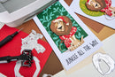 Card with a lion wearing a Santa hat and 'Jungle All The Way' text, surrounded by crafting tools on a wooden surface.