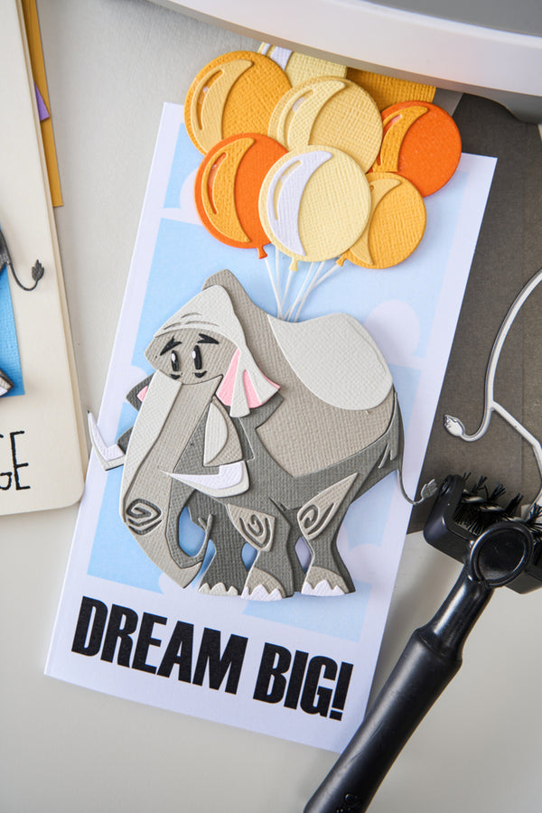 Card with an elephant holding balloons and 'Dream Big!' text on a white surface.