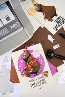 Personalized card with bear illustration and text, surrounded by craft materials and a printer.
