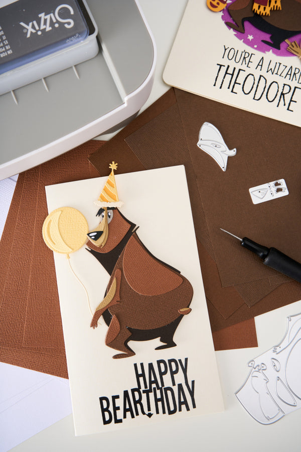 Card with bear design and 'Happy Bearthday' text on a crafting surface with tools.