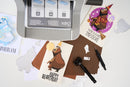Card-making setup with a printer, cut-out bear illustrations, and stationery on a white surface.