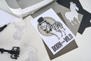 Card with zebra illustration and 'Born to be Wild' text on a desk with craft materials.
