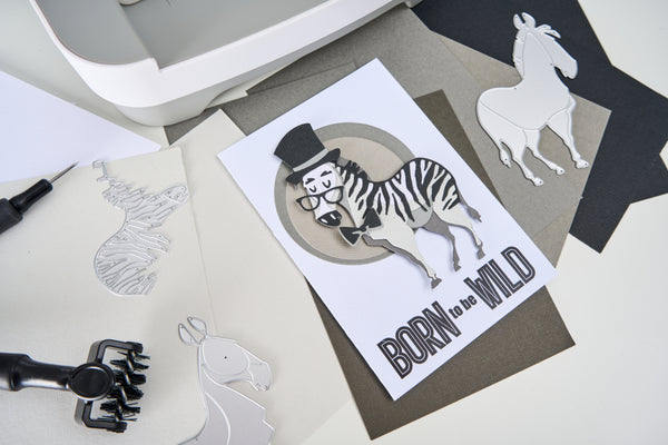 Card with zebra illustration and 'Born to be Wild' text on a desk with craft materials.