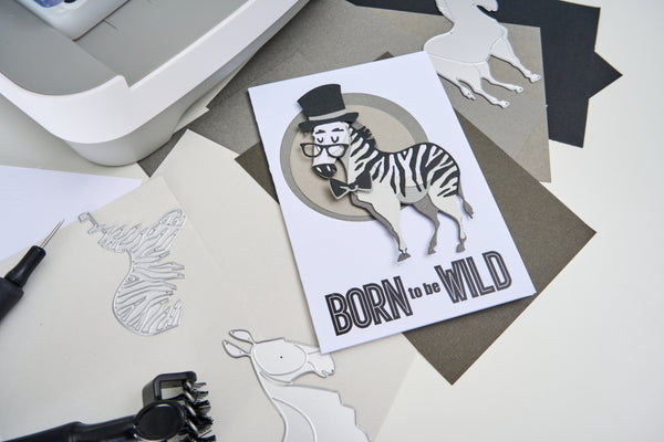 Card with zebra wearing a top hat and bow tie, text 'Born to be Wild', surrounded by paper cutouts on a light background.