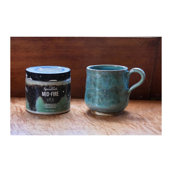 Ceramic mug and container labeled 'Mid-Fire Dragon Stone' on a wooden surface with a wooden panel background.