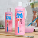 Two bottles of Speedball Pink Soap on a table with brushes and a glass of water.