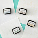 Four small rectangular containers with labels on a textured white surface.