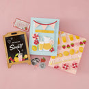 Collection of decorative items including a chalkboard sign, cards, and small figurines on a pink background.