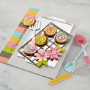 Colorful baking set with cookies, flowers, and utensils on a marble surface