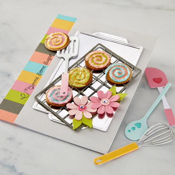 Colorful baking set with cookies, flowers, and utensils on a marble surface