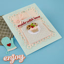Decorative card with 'made with love' text and cupcake illustration, accompanied by a small oven mitt on a blue background.