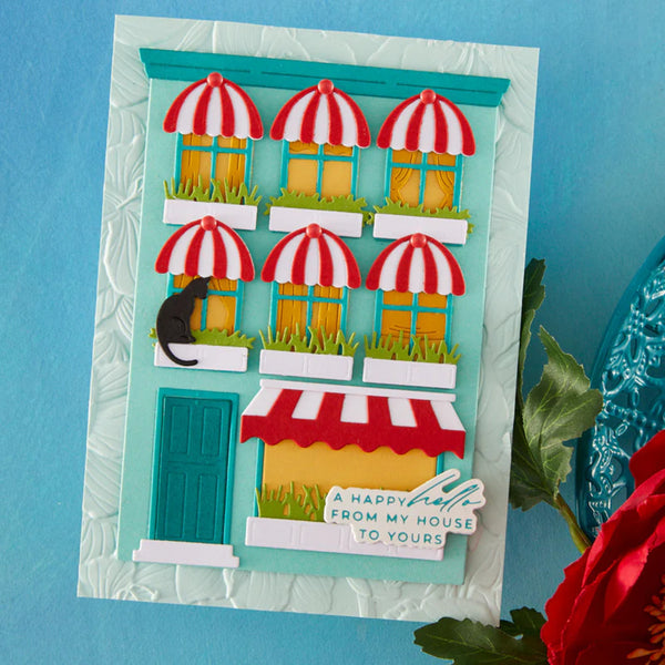 Handmade card with a colorful street scene featuring buildings and red and white striped awnings on a blue background.