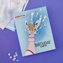 Birthday card with champagne bottle and cookie design on a purple background