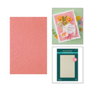 Pink textured paper with embossed designs, a card with flowers, and Spellbinders packaging on a white background.