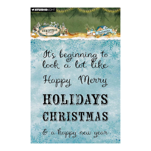 A Studio Light Christmas card with a watercolor blue background, black cursive and block lettering that reads 'It's beginning to look a lot like Happy Merry HOLIDAYS CHRISTMAS & a happy new year', with a green pine-treetop border and small holiday illustrations at the top.