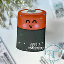 Battery-shaped container with a face and text 'need a recharge' on a blurred background.