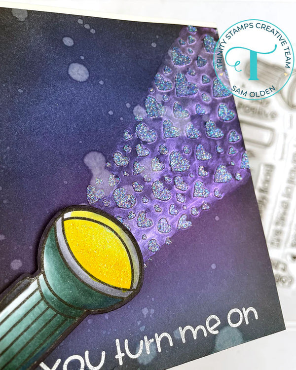 Card with a light bulb and purple hearts on a dark background, featuring 'Tombow Stamps Creative Team' logo.