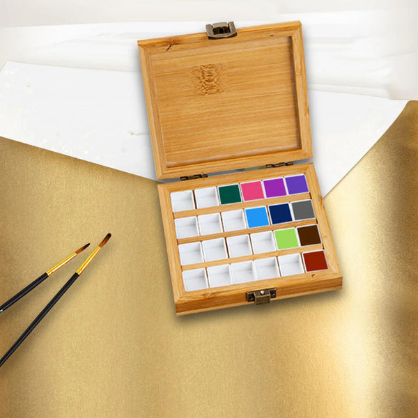 Wooden paint palette with watercolors and brushes on a gold surface