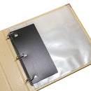 Black binder clip on a beige ring binder with clear sleeves.