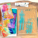 Art supplies including colorful abstract paintings and a stenciled design on brown paper.