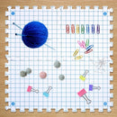 Grid-patterned mat with yarn ball, paper clips, and small items on a wooden surface