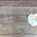 Clear baking mat with grid pattern on a wooden surface with decorative items.