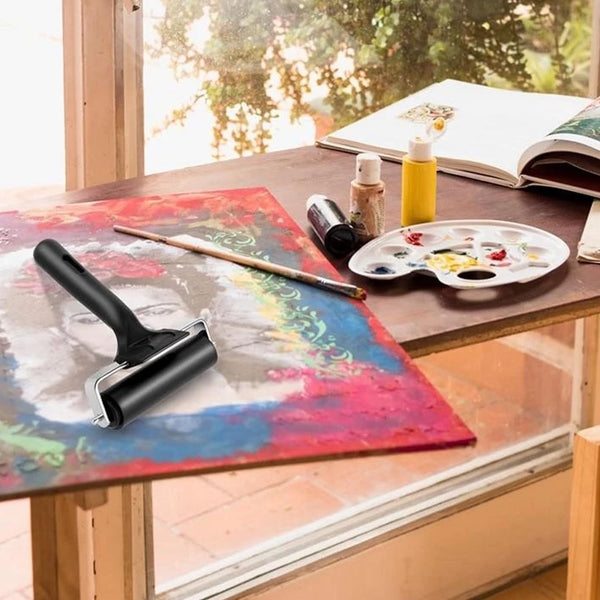 Artistic setup with a roller, paint bottles, and a palette on a table by a window.
