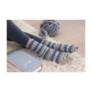 Striped socks being worn on a textured surface with yarn and a book in the background