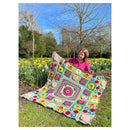 Person holding a colorful crocheted blanket in a garden with daffodils.
