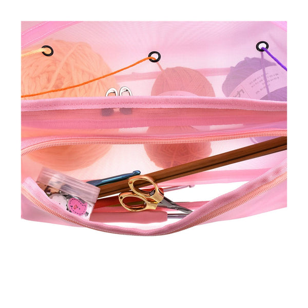 Pink knitting bag with yarn, needles, and scissors on a white background