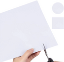 Hand holding scissors about to cut a piece of white paper with a small square cutout on a white background.
