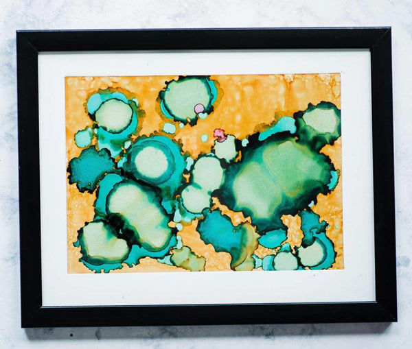 Framed abstract artwork with green and blue patterns on a yellow background